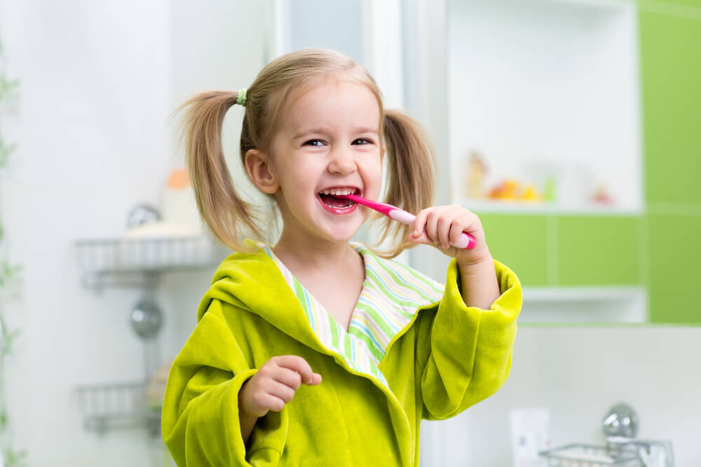 Smiling kid girl brushing teeth in bathroom